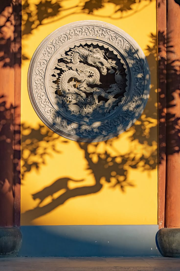 the shadow of a tree is cast on a wall with a decorative plate in front of it