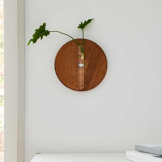 a wooden clock mounted to the side of a white wall with a plant in it