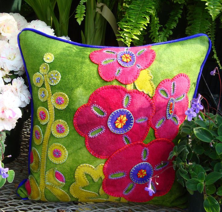 a green and pink pillow sitting on top of a chair next to some white flowers