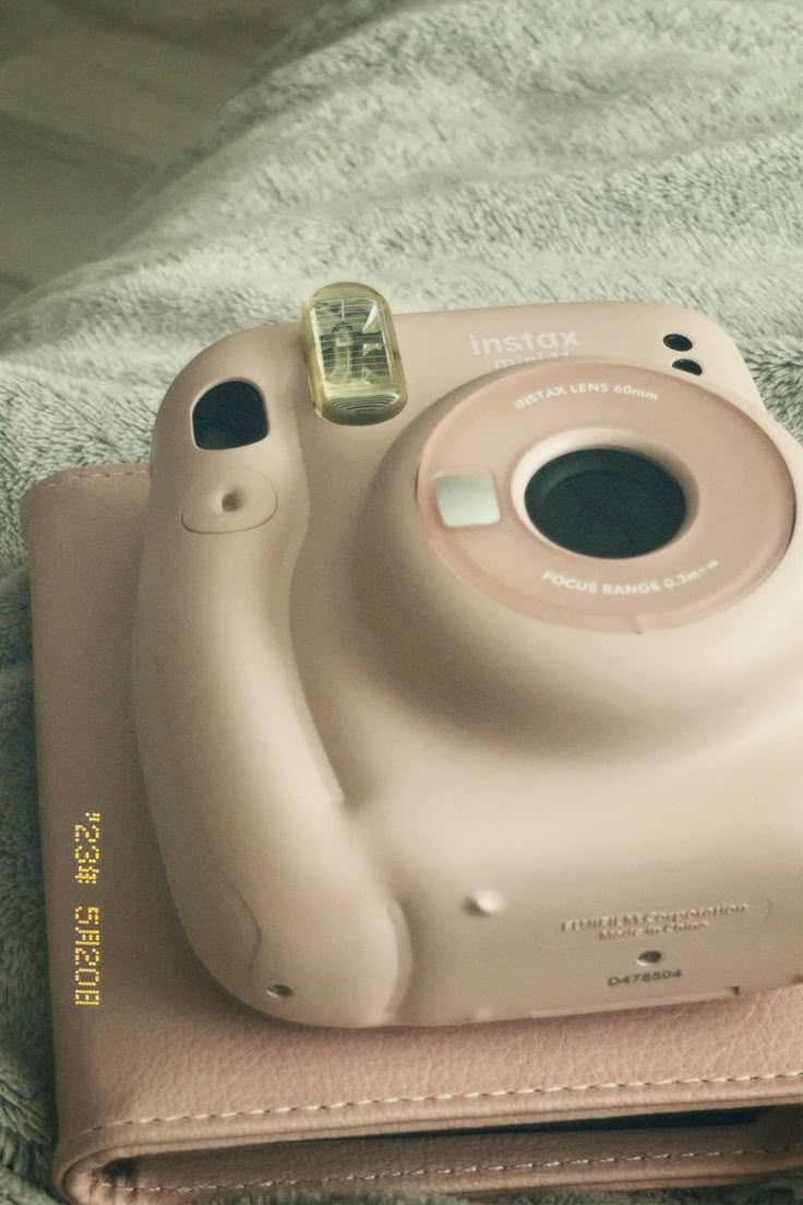 a camera sitting on top of a pink case next to a white towel with a gold button