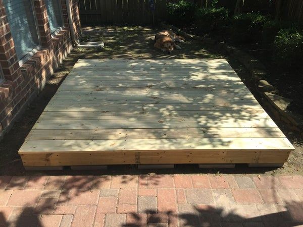 a dog laying on top of a wooden platform in the back yard next to a brick wall