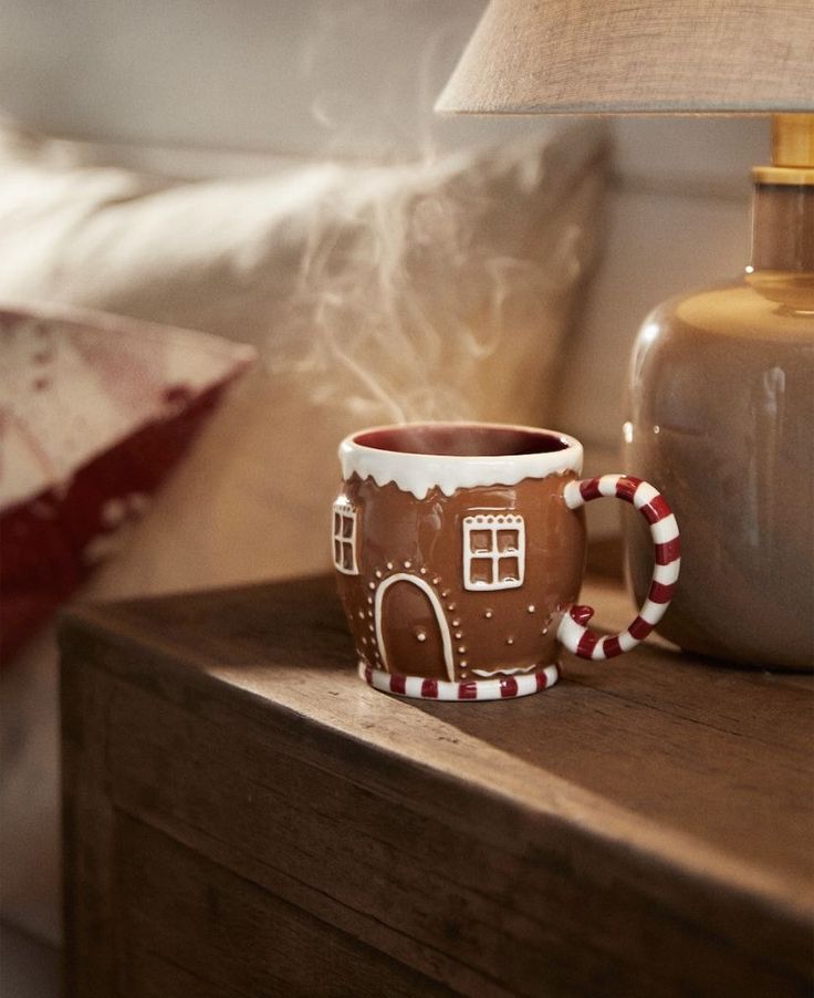 a coffee mug sitting on top of a wooden table next to a lamp and pillow