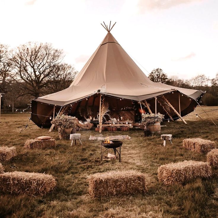 a teepee tent with hay bales in the foreground and tables set up outside