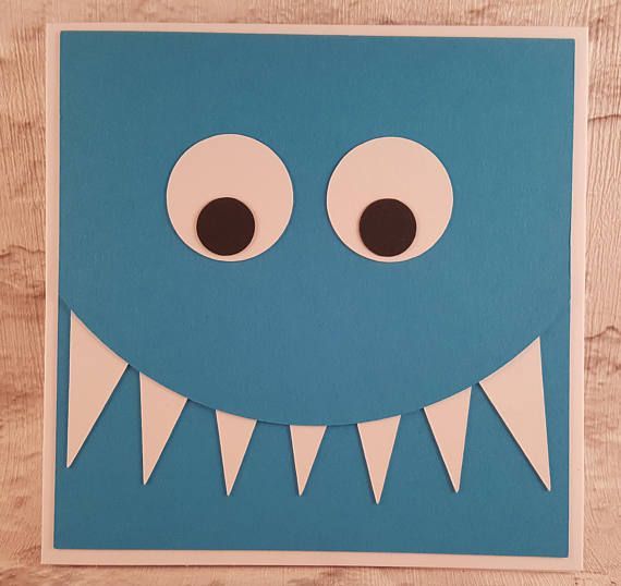 a blue monster card with large eyes and sharp teeth, cut out from paper on a wooden surface