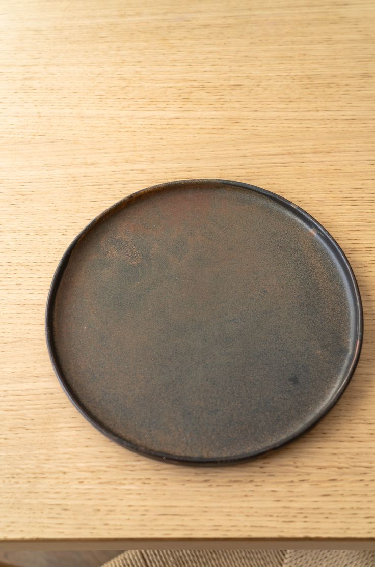 a black plate sitting on top of a wooden table next to a brown cloth bag