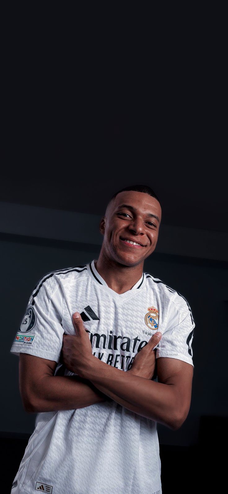 a man is posing for a photo in his soccer uniform with his arms crossed and smiling at the camera