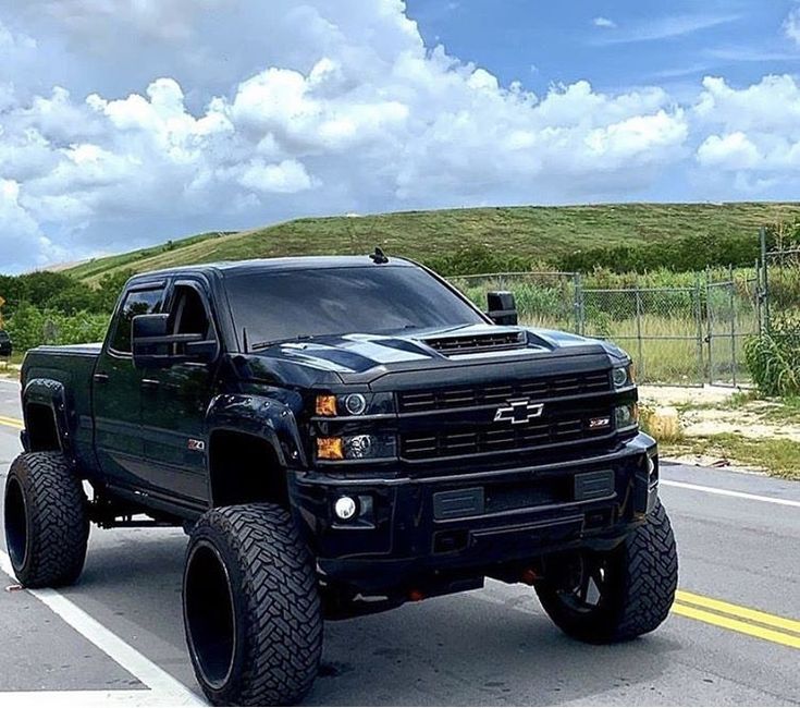 a black truck driving down the road with big tires on it's front wheels