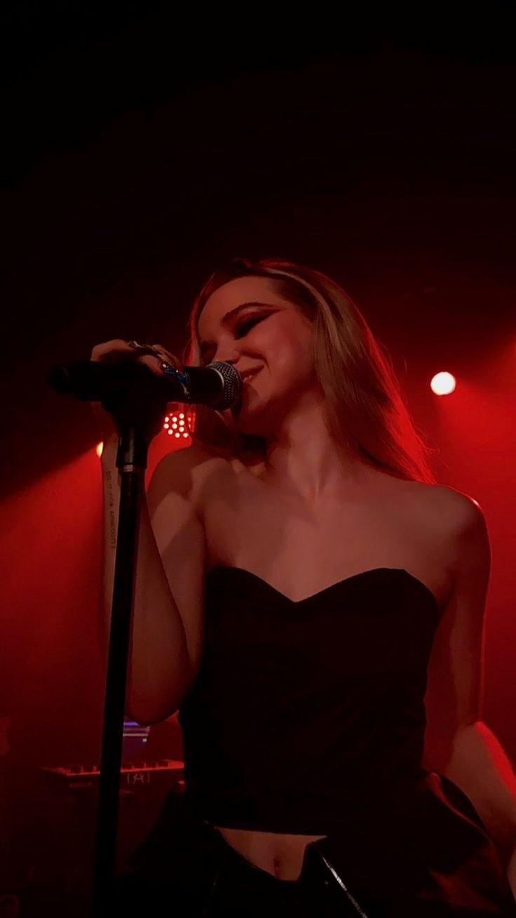 a woman in a black dress singing into a microphone on stage with red lights behind her