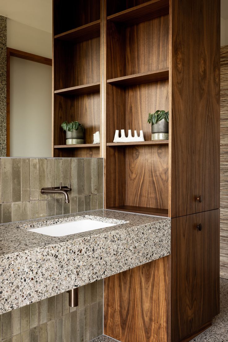 a bathroom sink sitting under a mirror next to a wooden shelf filled with potted plants