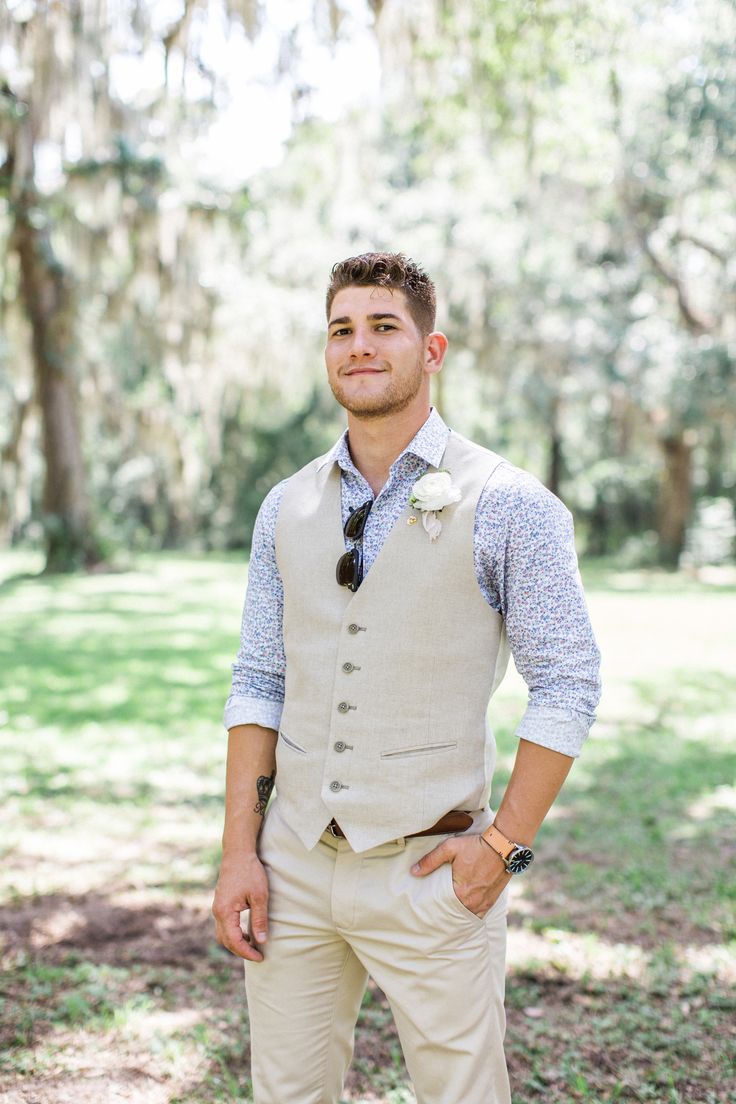 a man standing in the grass wearing a vest and tie with his hands on his hips