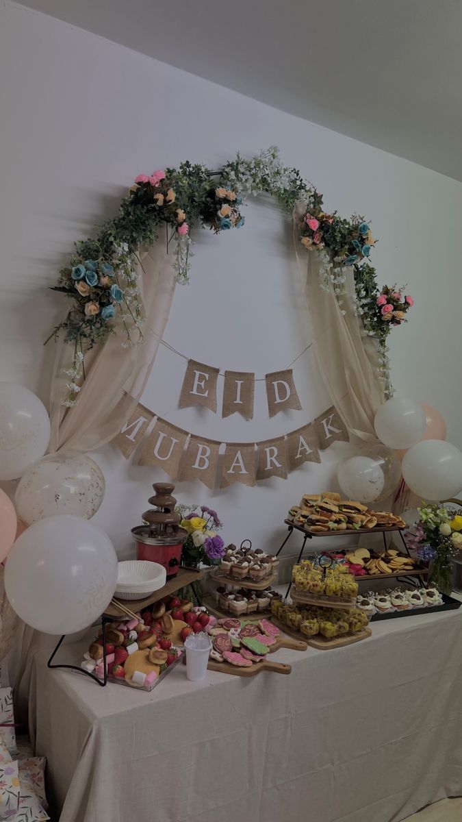 a table topped with lots of desserts and balloons next to a sign that says eid lubara