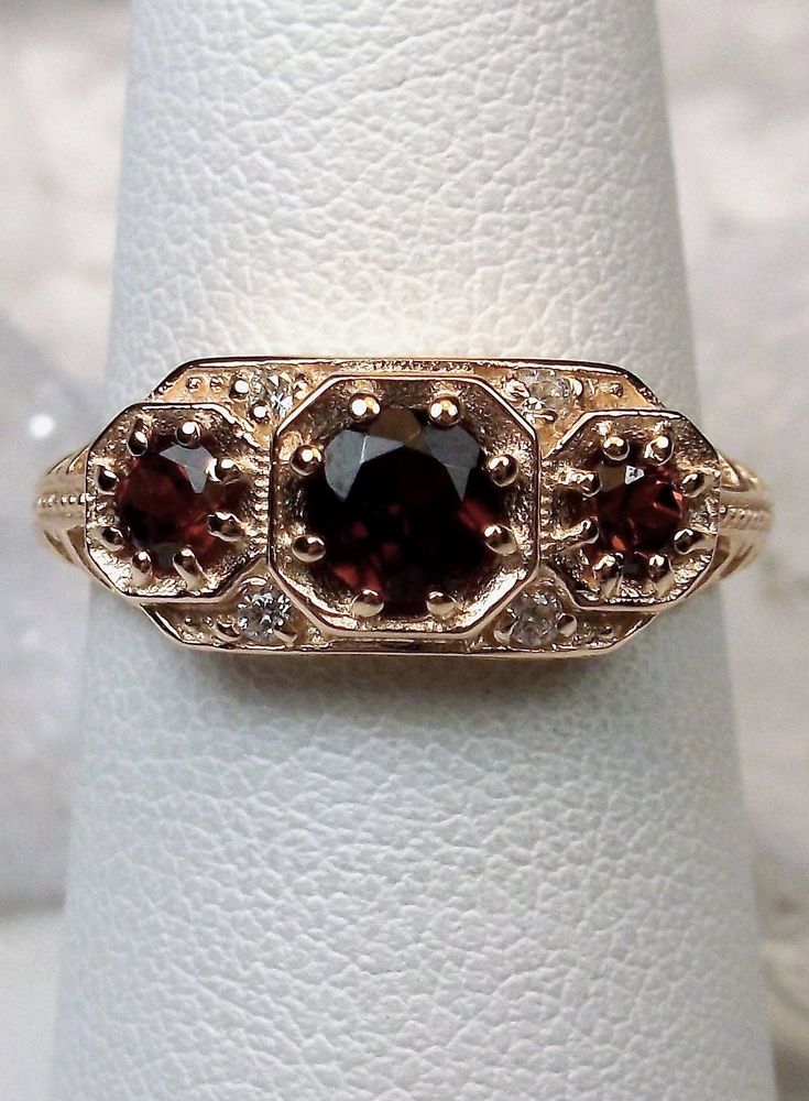 Natural Red Garnet Ring Description  Dainty 3Stone Design#161 Custom This is a high-quality Edwardian reproduction filigree ring in 14K rose gold. This filigree 3 stone ring is set with 3 genuine natural red garnet gemstones. The oval full cut red garnet in the center is 4.5mm. The 2 garnets on each side are 2.5mm. The face of the ring is 15.5mm (5/8th") east-west on the finger and 7mm (1/4th") north-south on the finger. The inside of the band is marked 14K for gold. Notice the beautiful filigre Rose Gold Art, Art Deco Filigree, Red Garnet Ring, Garnet Jewelry, Gold Art Deco, Garnet Ring, Rose Gold Band, North South, Filigree Ring