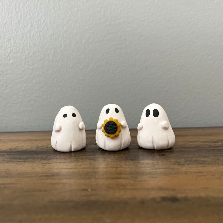 three small white ghost figurines sitting on top of a wooden table