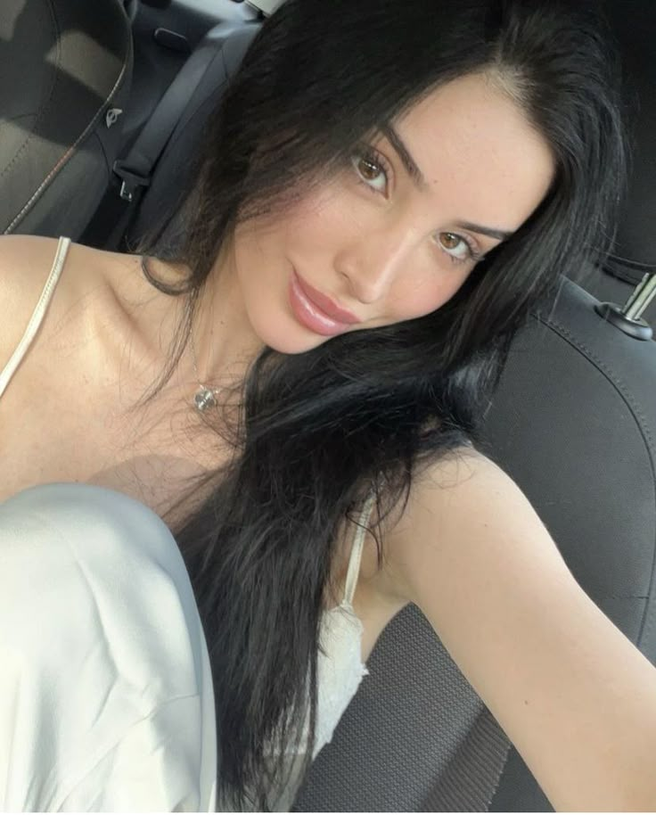 a woman sitting in the back seat of a car with long black hair on her head