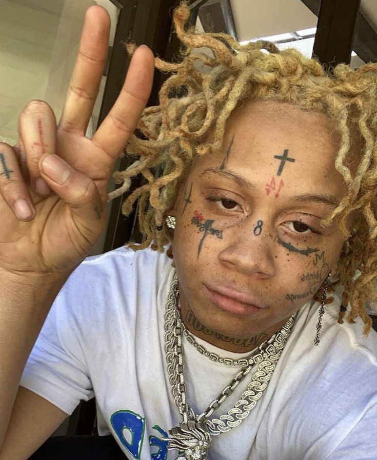 a woman with dreadlocks and tattoos on her face making the peace sign gesture