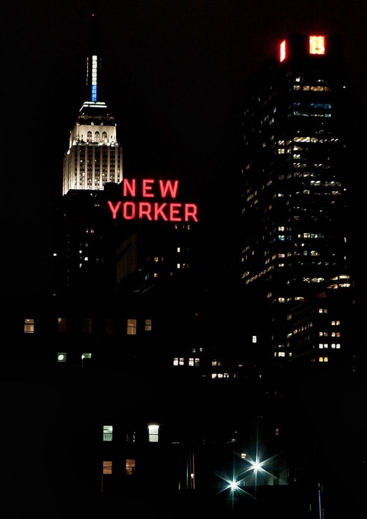 the words new york are lit up at night in front of tall buildings and skyscrapers