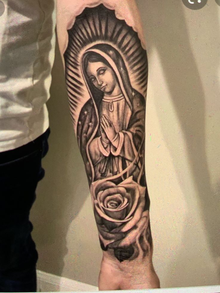 a person with a tattoo on their arm holding a rose and an image of the virgin mary