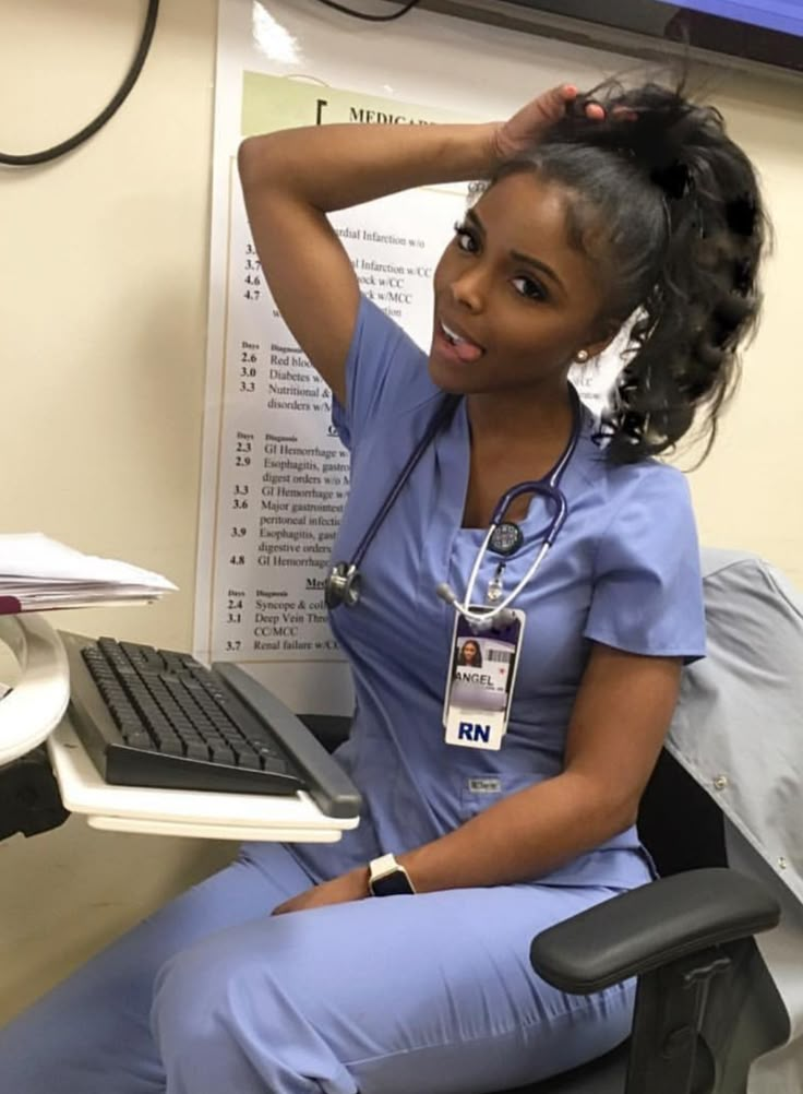 a woman in scrubs sitting at a computer desk