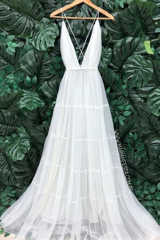 a white dress hanging on a wooden hanger in front of a green leafy wall