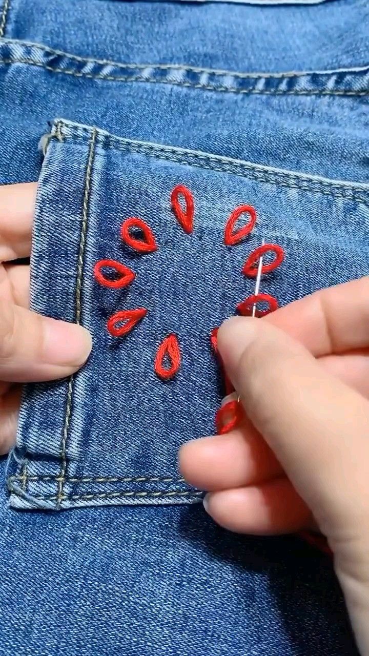 someone is stitching the holes in their jeans with red thread and pins to make them look like lips