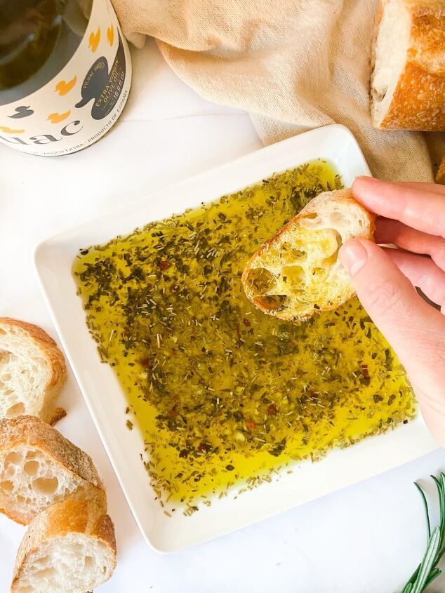 a person is dipping pesto into bread on a white plate next to garlic bread