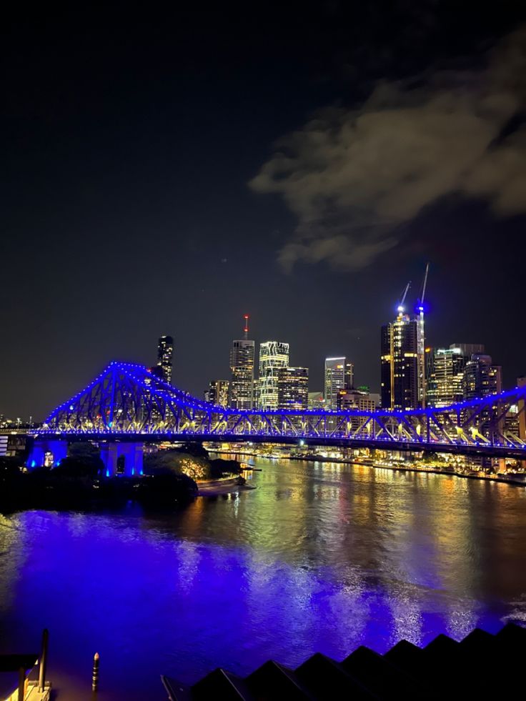 the city skyline is lit up at night with blue lights on it's bridges