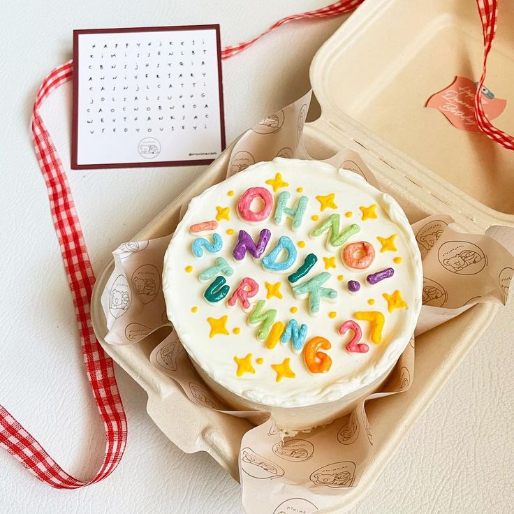 a birthday cake sitting on top of a box next to a red and white ribbon