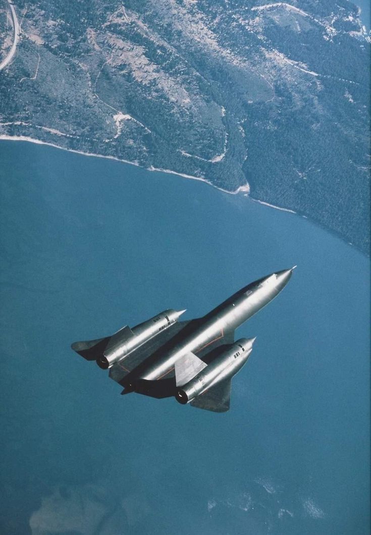 two fighter jets are flying in the sky above some water and land, with mountains in the background