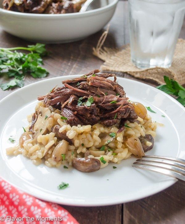 a white plate topped with rice covered in meat and mushrooms next to a glass of water