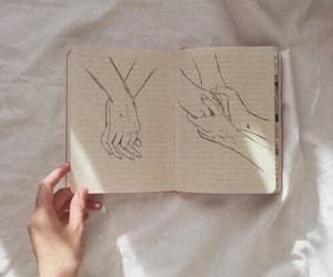 two hands holding each other's hand over an open book on top of a bed