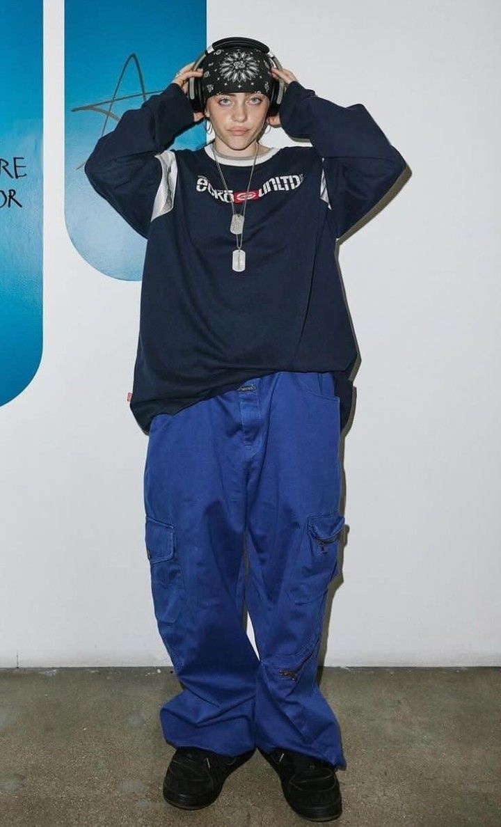 a man standing in front of a wall with his hands on his head and wearing blue pants