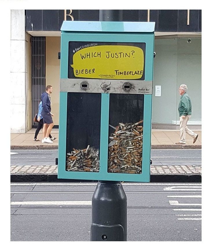 a trash can sitting on the side of a street next to a pole with a sign that reads which justtin?