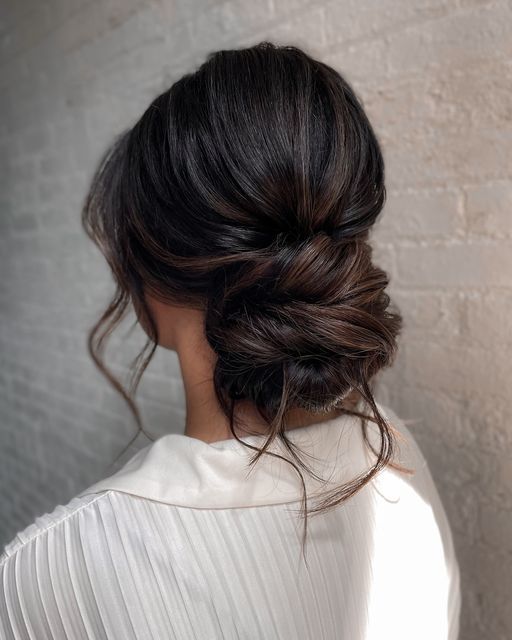 a woman with dark hair wearing a white top and braided up in a low bun