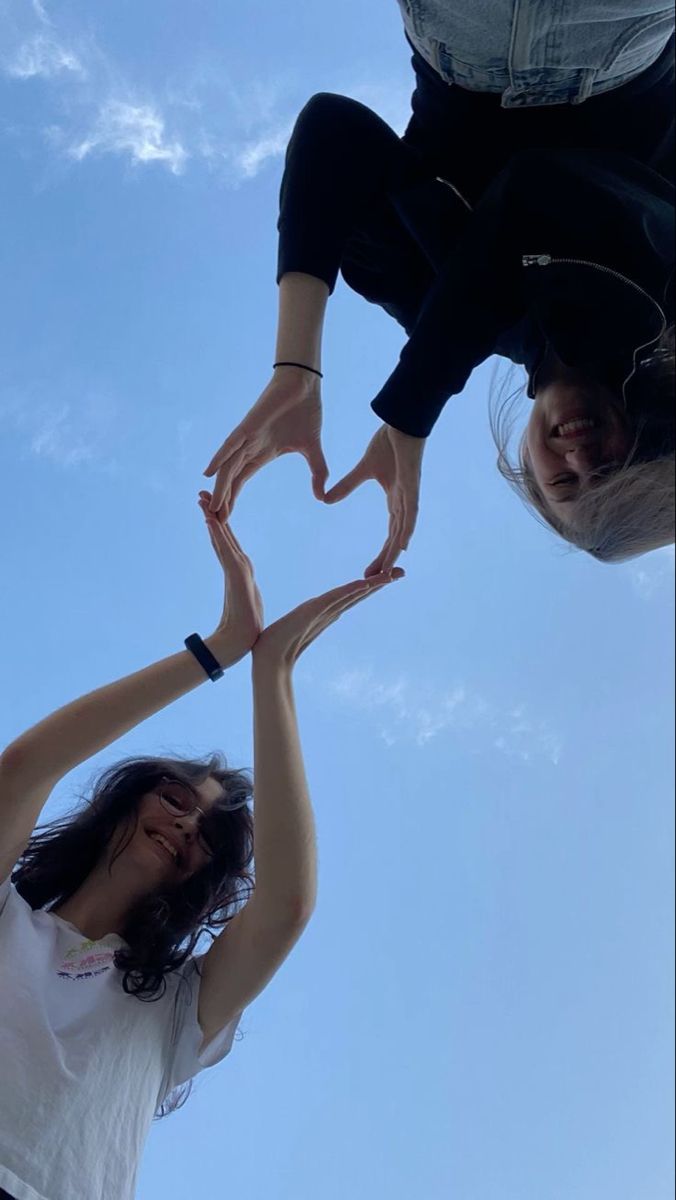 two people reaching up into the air with their hands in the shape of a heart