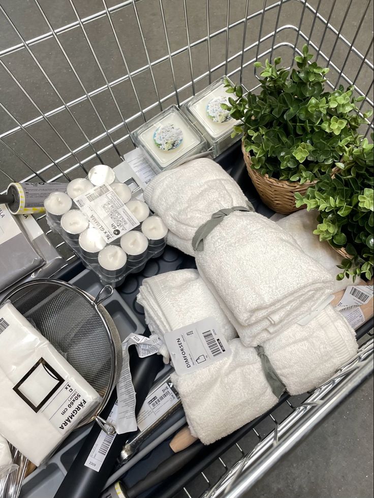 a shopping cart filled with lots of white towels and other bathroom items next to a potted plant