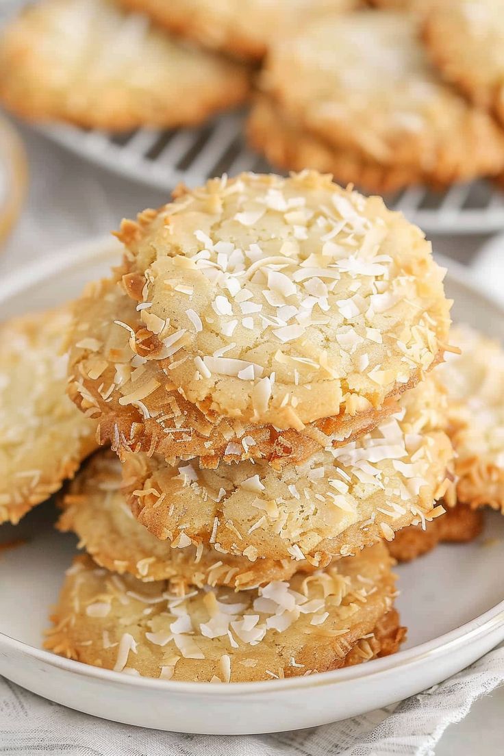 coconut cookies stacked on top of each other in a white plate next to more cookies