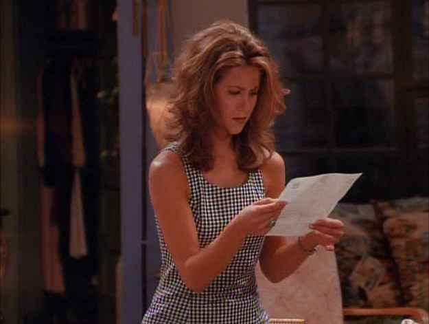 a woman standing in front of a table holding a piece of paper and looking at it