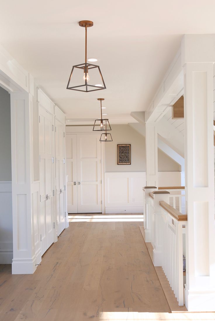 an empty hallway with white walls and wood flooring on the other side is a light fixture that hangs from the ceiling