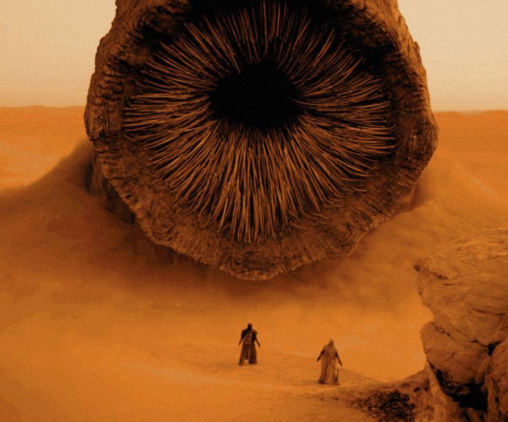 two people are standing in the desert near a rock formation with an eye on it