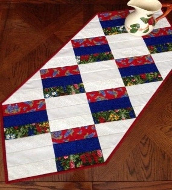 a quilted table runner on the floor with a tea pot and pitcher sitting next to it