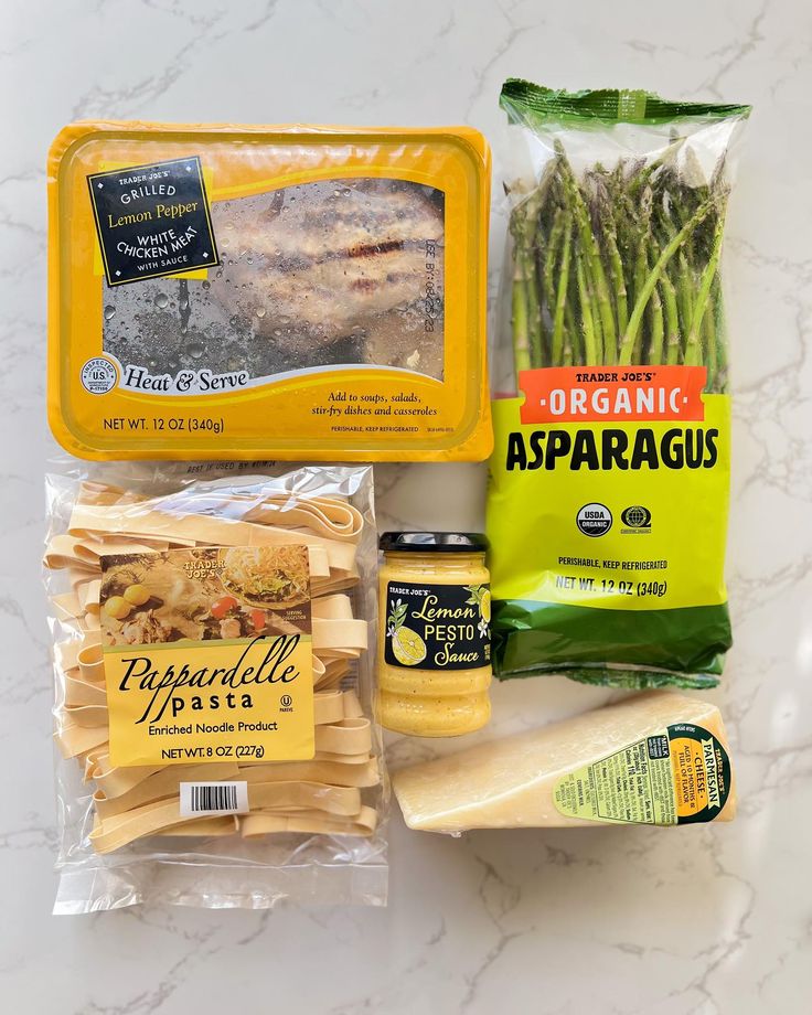 an assortment of pasta, asparagus, cheese and seasoning on a marble surface