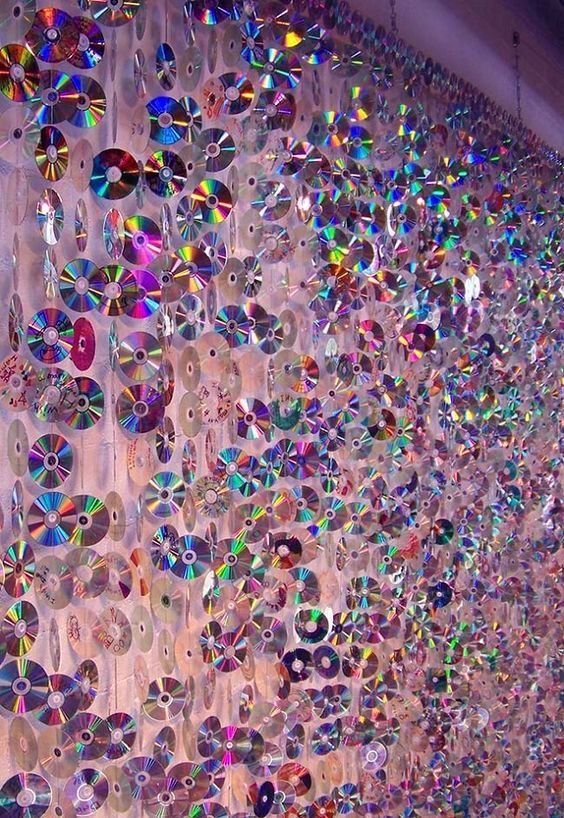 many cds are hanging on the wall in front of a window with iridescent colors