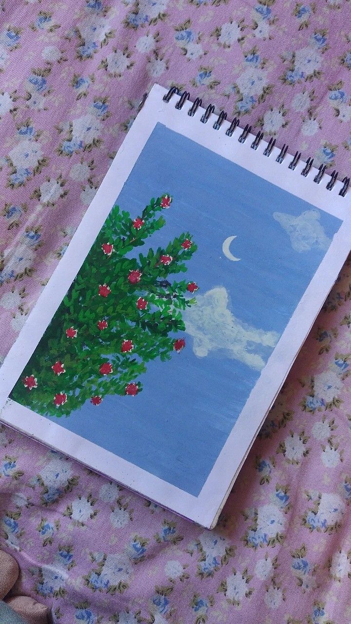 an open notebook with a drawing of a christmas tree on it sitting on a bed