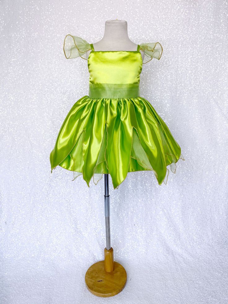 Carefully hand stitched together with the upmost care, this dress will make the perfect unique Halloween costume! Beautifully handcrafted Tinkerbell inspired dress made out of satin; A sleek satin top with spaghetti straps and attached sheer sleeves. The front bodice has a waist belt that does not extend to the back and can be decorated with your own flower. Zipper can be found at the back of the bodice. Knee length skirt made out of sheer and satin strips of fabric that creates a fairy-like sil Fairy Tinkerbell, Spaghetti Strap Gown, Tinkerbell Fairies, Toddler Birthday Party, Fairy Festival, Party Photoshoot, Unique Halloween Costumes, Photoshoot Props, Green Gown