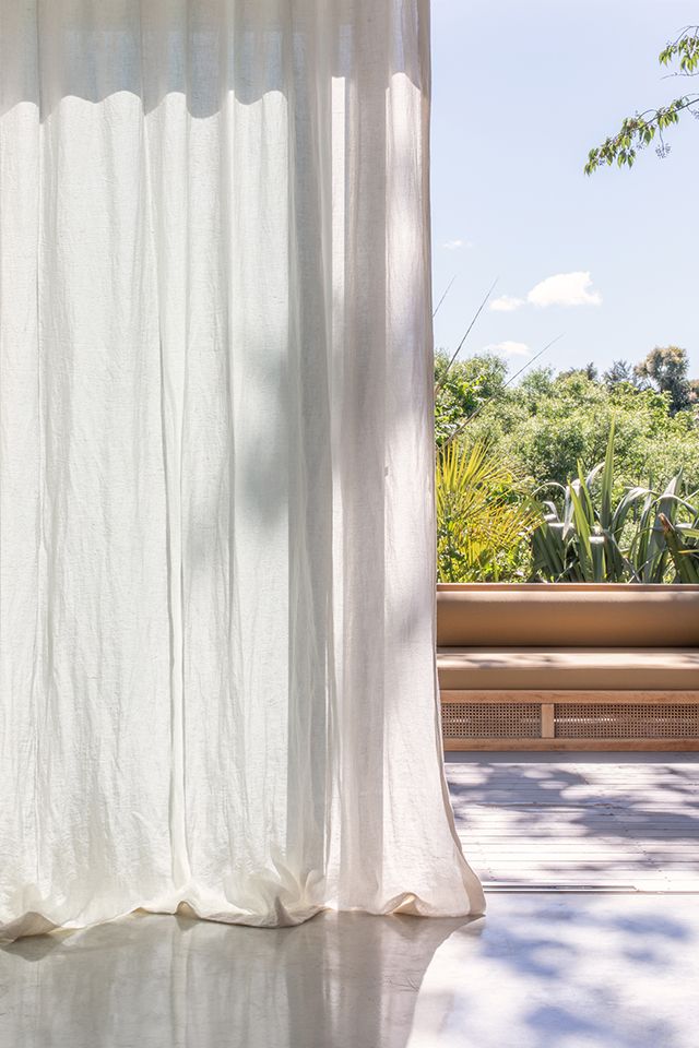 an open window with white curtains and plants in the background