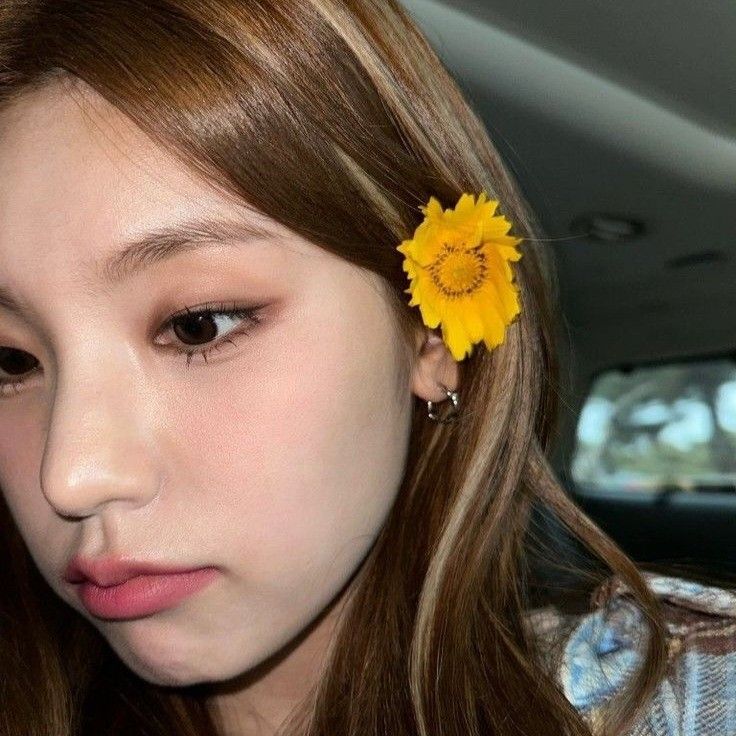 a girl with long brown hair and a yellow flower in her hair is looking at the camera