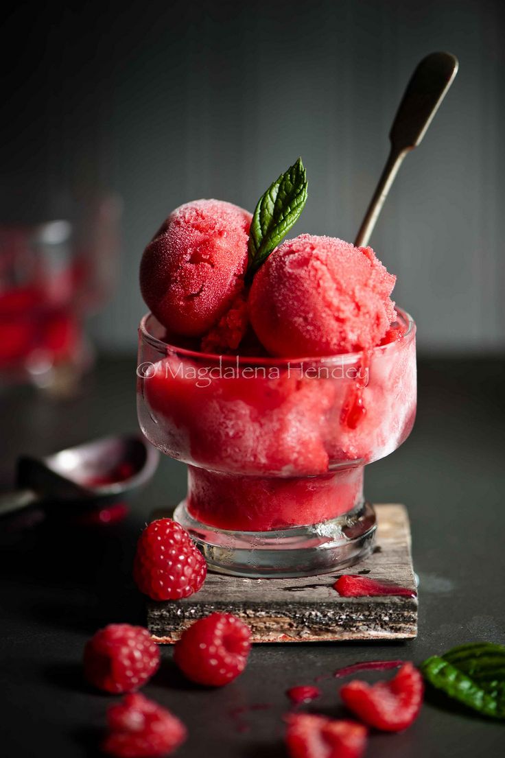 two scoops of ice cream with raspberries in a glass bowl on a table