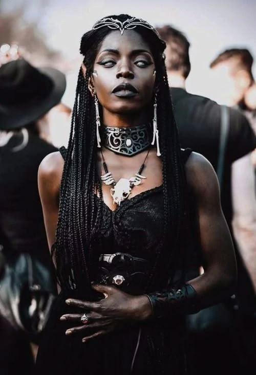 a woman with black makeup and braids standing in front of other people wearing hats