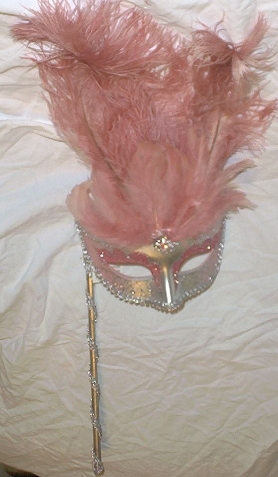 a masquerade with pink feathers on top of a white sheeted bed spread