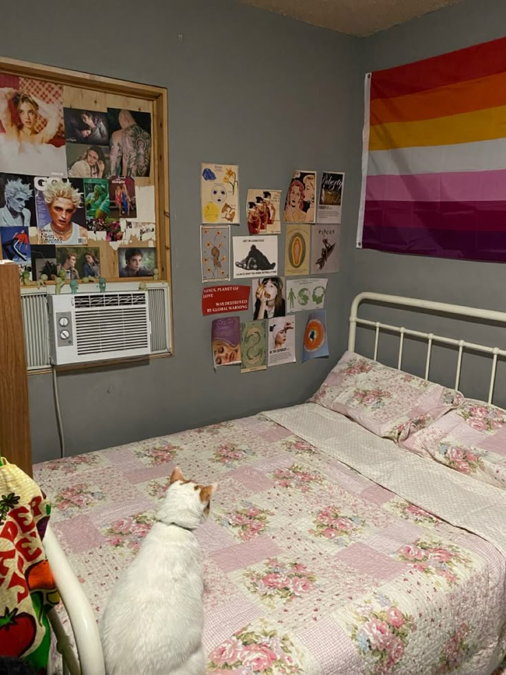 a white cat sitting on top of a bed next to a wall with pictures and posters